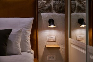 A bedroom with a bed, a nightstand, a wall-mounted light, a power outlet, and a wooden shelf.