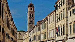 Una calle histórica con edificios de arquitectura clásica, una torre destacada con cúpula y banderas que señalan una ubicación europea.