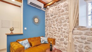 Una sala de estar con pared azul, pared de piedra, techo de madera, un sofá, una pequeña mesa redonda con una botella y vasos, y una cortina.