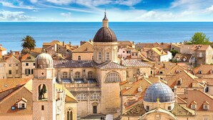 Un paisaje urbano costero con arquitectura histórica, incluyendo edificios con cúpulas y construcciones de tejas a la española.