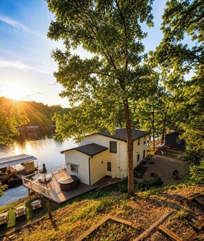 A lakeside cabin with a deck, a small outdoor seating area, and a view of the water.