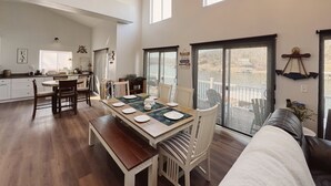 A spacious living area with a dining table set for four, a large window overlooking a balcony, and a cozy seating area with a sofa and a bench.