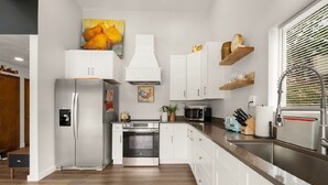 A modern kitchen with white cabinets, stainless steel appliances, and a wooden floor.