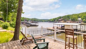 A wooden deck with chairs overlooking a lake with boats, surrounded by greenery and hills.