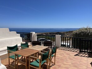 A terrace with a wooden table and green chairs, overlooking a rocky coastline and the ocean. - Stunning sea views near the beach (Son Parc)
