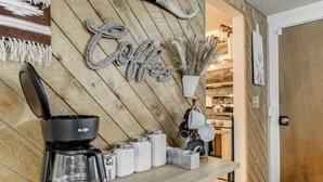A coffee station with a coffee maker, milk frothing pitcher, and various coffee containers on a wooden table. - Come to the Hideout! Hot Tub, Fire Pits & Views! (Woodland Park)