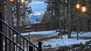 A snowy outdoor area with a wooden fence, trees, and a birdhouse. - Come to the Hideout! Hot Tub, Fire Pits & Views! (Woodland Park)