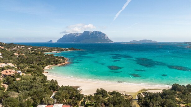 Eine Küstenlandschaft mit einem markanten Berg, klarem türkisblauem Wasser und einem Sandstrand.