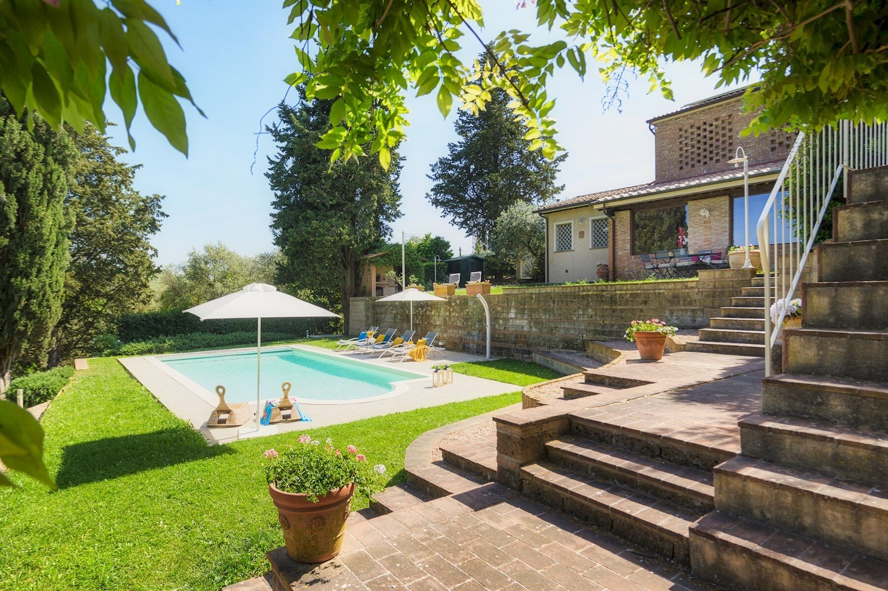 Ein Garten mit Swimmingpool, einer Terrasse mit Gartenmöbeln und einer Treppe, die zu einem Haus führt.