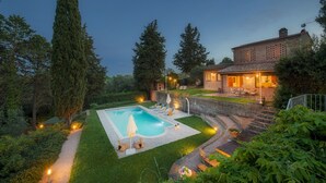 A private pool area with a small deck, surrounded by a well-maintained lawn and tall trees.