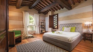 A bedroom with a large bed, a green chair, a window with curtains, a bookshelf, and a wooden ceiling.
