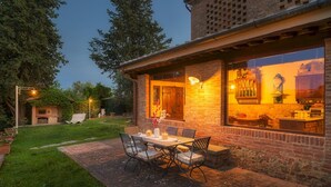 A patio with a table and chairs, a brick fireplace, and a view of a kitchen through large windows.
