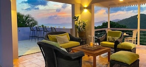 A covered outdoor seating area with wicker furniture, a table, and a potted plant.
