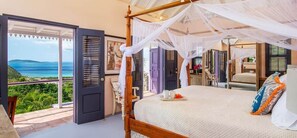 A bedroom with a four-poster bed, a balcony with a view of the sea, and a tropical-themed decor.