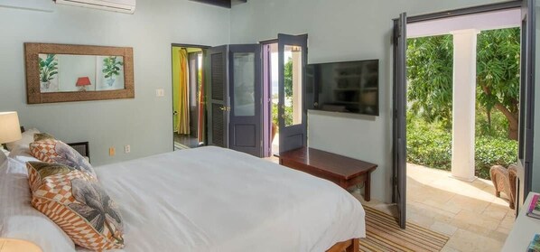 Une chambre à coucher comprenant un lit, une télévision, un bureau et une porte-fenêtre coulissante donnant sur un balcon.