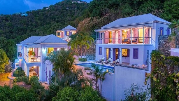 A multi-story house with a pool, surrounded by lush greenery and hills.