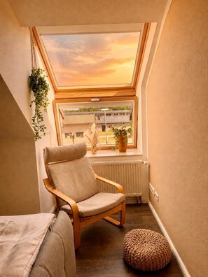 A cozy room with a skylight, a wooden chair, a small ottoman, and a radiator. - "Hofidylle" Vacation Apartment on a Pasture Farm (Beelitz)