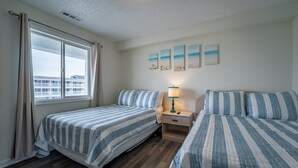 Una habitación con dos camas, una mesita de noche, una lámpara y un ventanal con cortinas.