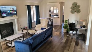 Una sala de estar moderna con un sofá azul, una chimenea, un televisor y una cocina al fondo.