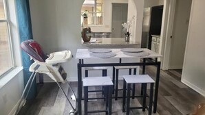 Una cocina con una mesa de comedor y sillas, una trona para bebé y una ventana con cortinas.