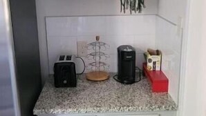 Cocina compacta con encimera de granito, cafetera, tostadora y un refrigerador pequeño.