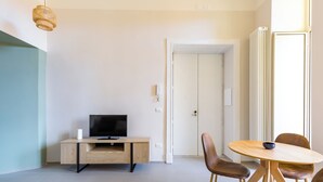 Ein modernes Wohnzimmer mit einem Flachbildfernseher auf einem Holztisch, einem runden Holztisch mit Stühlen und einer Tür zu einem weiteren Raum.