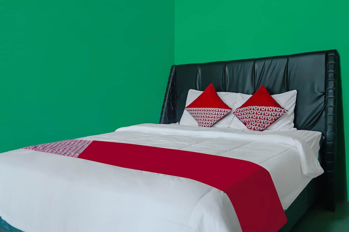 Un lit recouvert d’une couvre-lit blanche et rouge, deux oreillers rouges ornés de motifs blancs, et une tête de lit noire sur un mur vert.