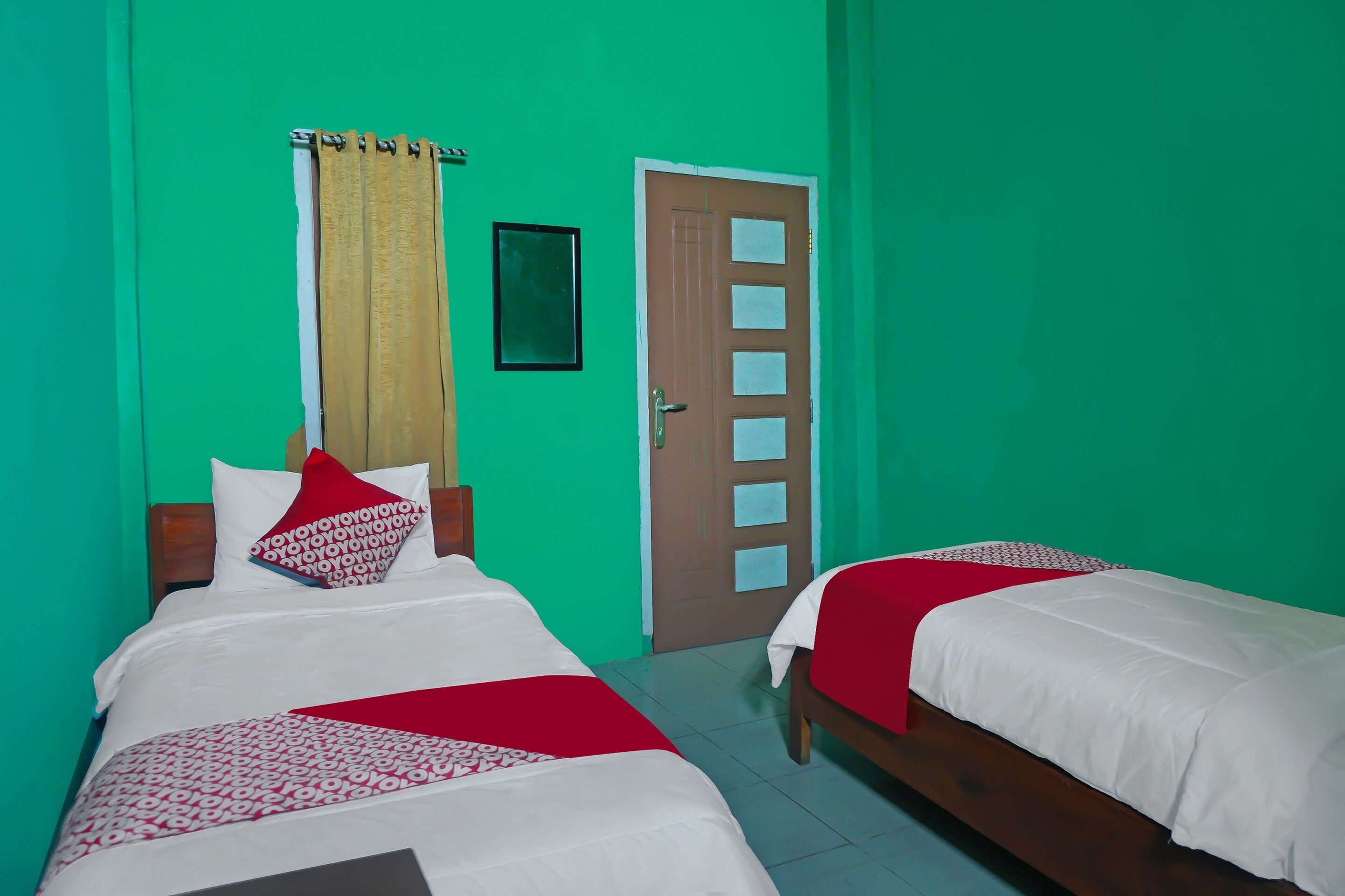 A room with two beds, green walls, a wooden door, and a window with curtains.