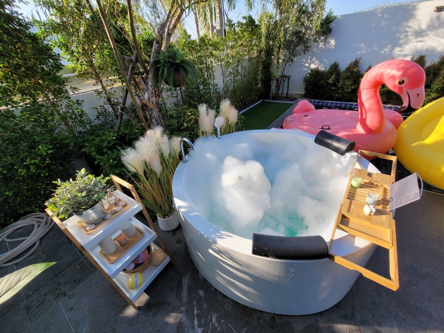 Un jacuzzi rodeado de plantas e flamencos inflables.