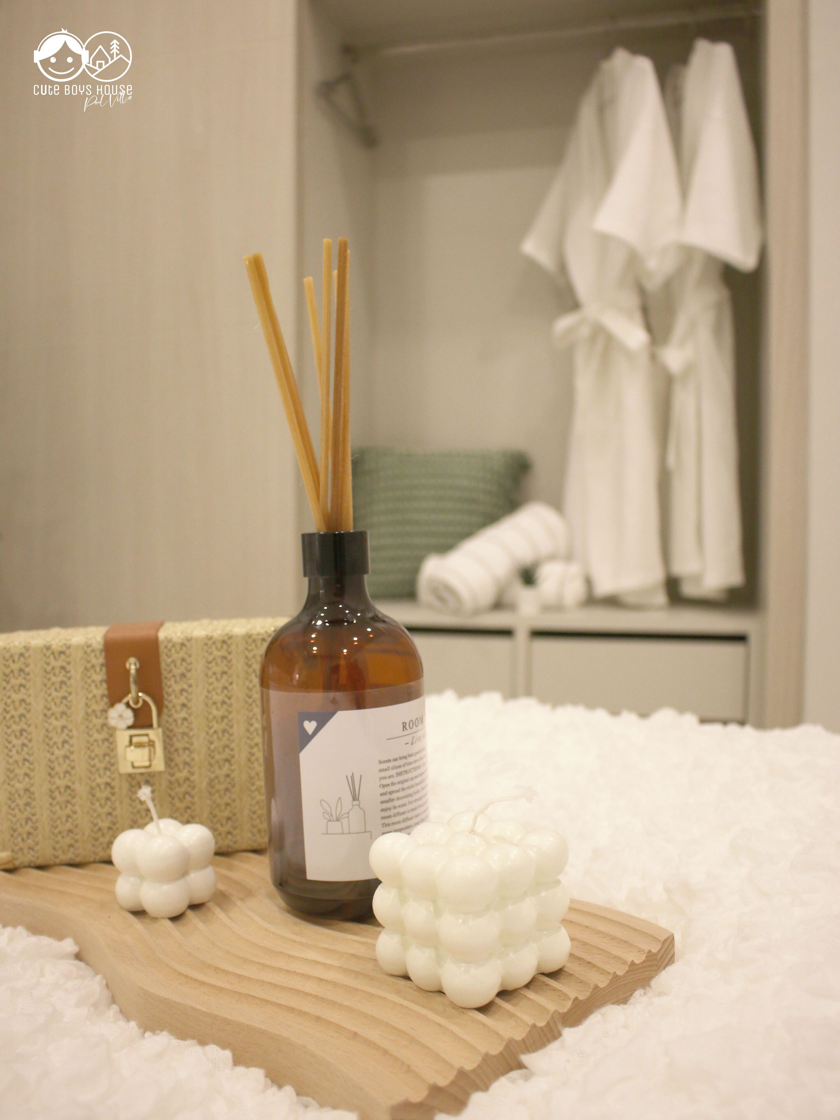 A bathroom with a bottle of reed diffuser, a white fluffy bath mat, and a towel rack with white towels.
