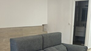 A grey sofa with a wooden headboard in a room with light wooden flooring and white walls. - New apartment in the center silver ground floor 2 rooms (Elche)
