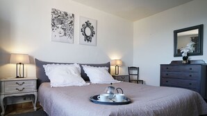 Een net opgemaakt bed met een dienblad met kopjes en een theepot, twee bedlampen, een kaptafel en twee decoratieve wandobjecten.