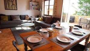 Een eetruimte met een houten tafel voor vier personen, een bank en een boekenkast in een goed verlichte kamer met uitzicht op het buitengebied.