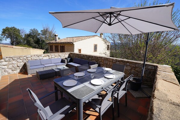 An outdoor patio with a dining table set for six, surrounded by wicker furniture and a large umbrella. - Le Reflet des Collines. Gateway to the Verdon. (Fox-Amphoux)