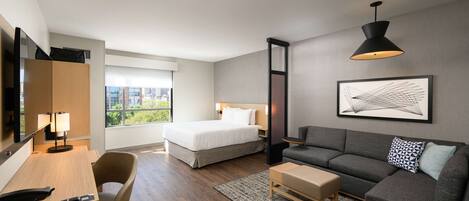 Een moderne hotelkamer met een bed, een bank, een bureau en een groot raam.