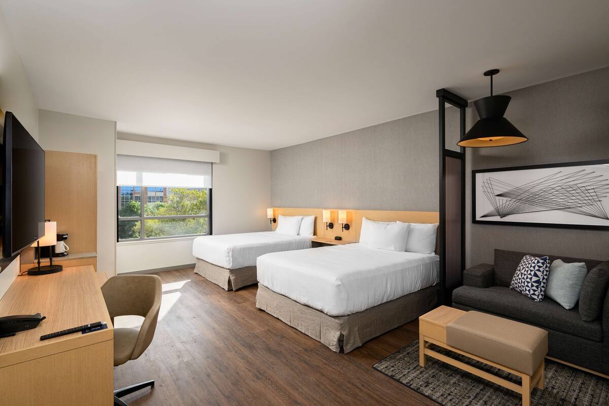 A hotel room with two beds, a desk, a TV, and a sofa.