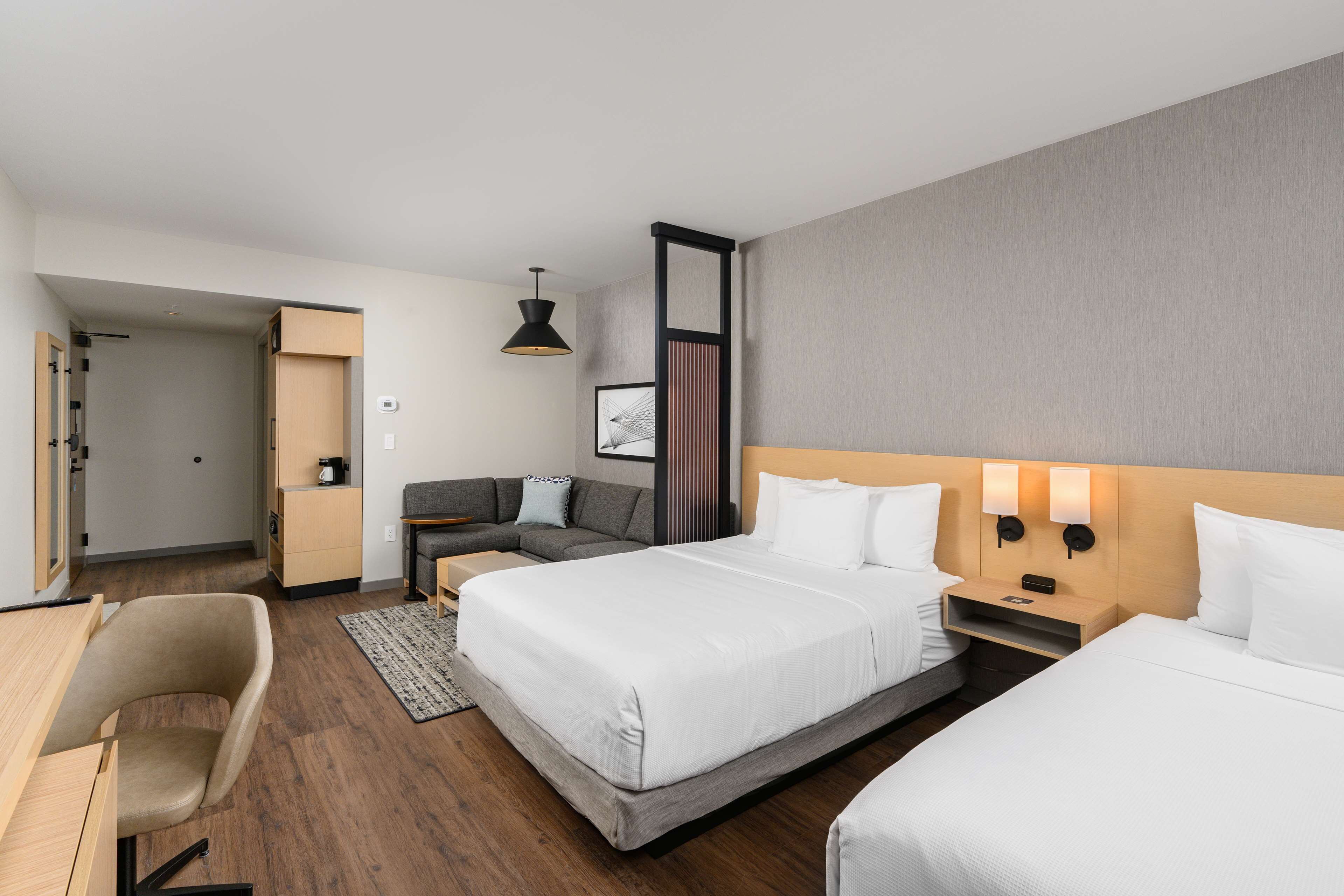 A hotel room with two beds, a desk, a chair, a sofa, and a bedside table with lamps.