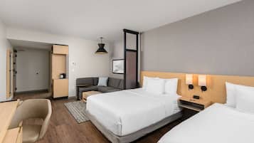 A hotel room with two beds, a desk, a chair, a sofa, and a bedside table with lamps.