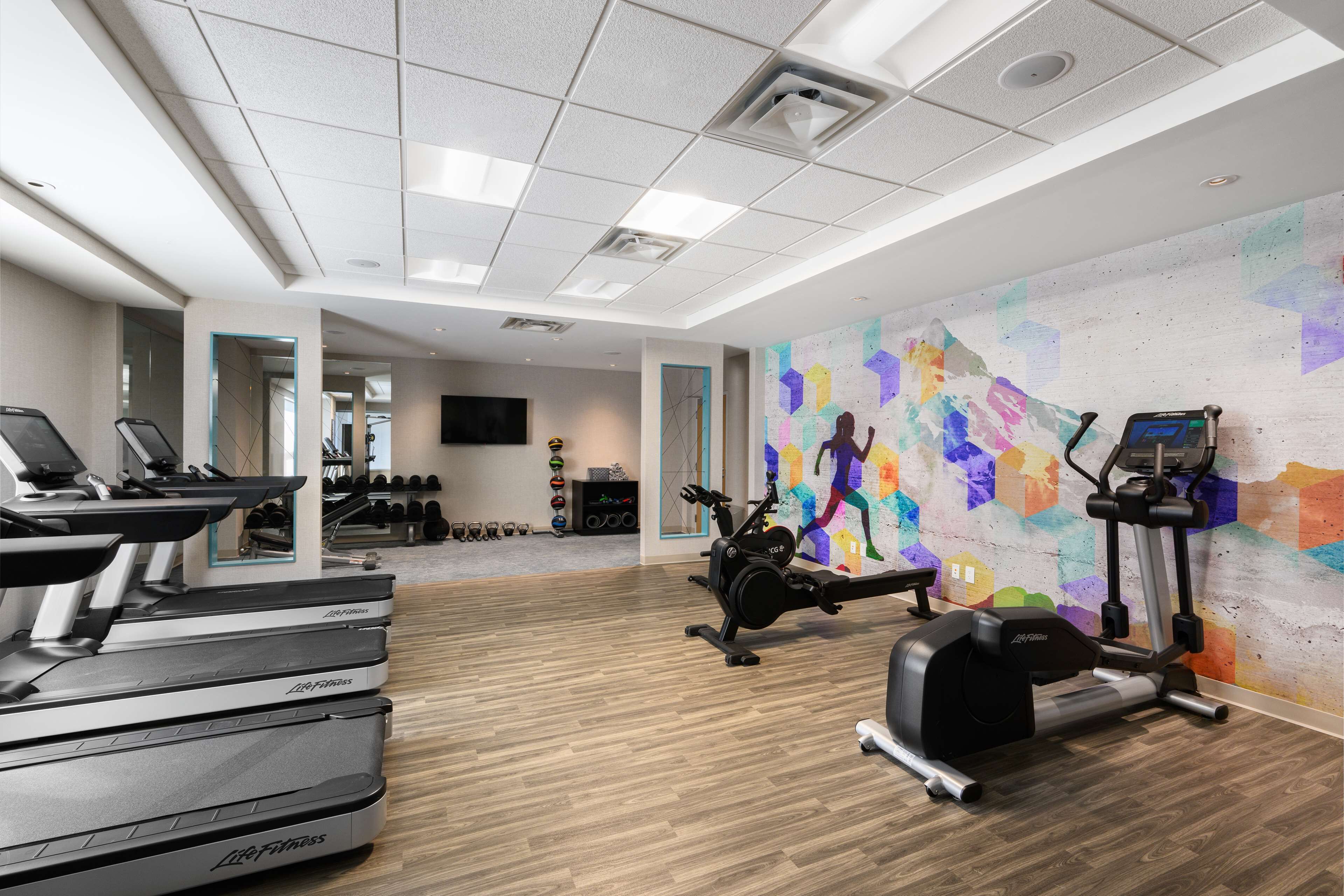 A gym with treadmills, an elliptical, and a colorful mural on the wall.