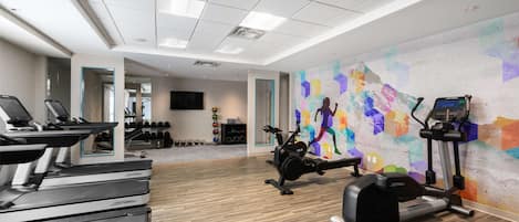 A gym with treadmills, an elliptical, and a colorful mural on the wall.