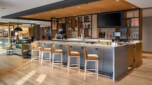 A modern bar area with a wooden ceiling, a large TV screen, and a bar counter with stools. - Hyatt Place Albany/Downtown (Albany)