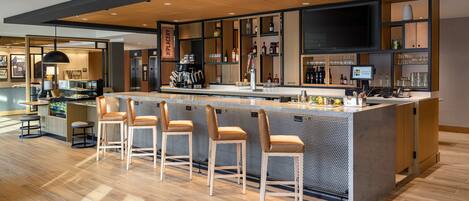 Zona de bar moderna con techo de madera, una pantalla de televisión grande y una barra con taburetes.