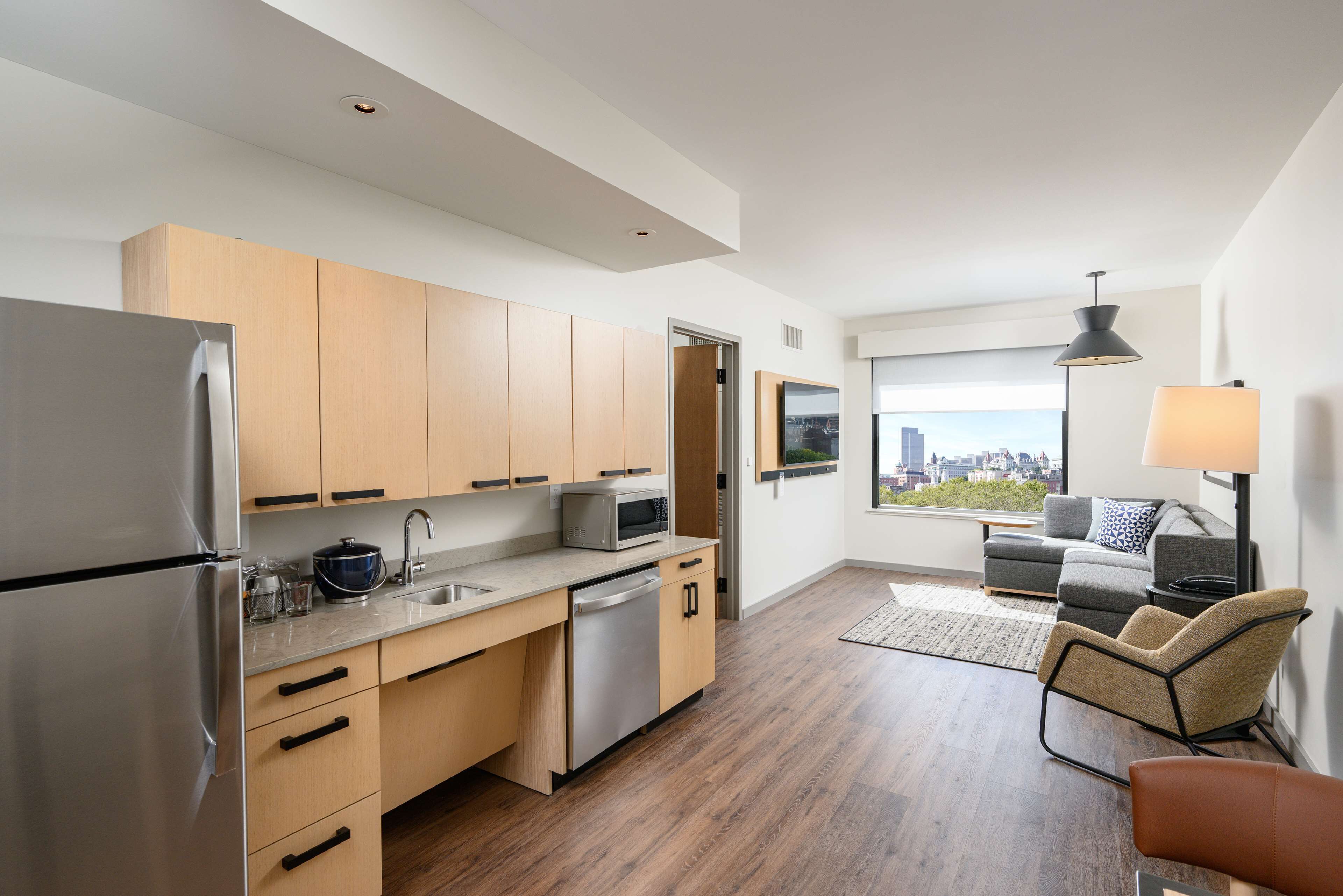 A modern kitchen with wooden cabinets, stainless steel appliances, and a view of the city through large windows.