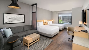 A modern hotel room with a grey sofa, two single beds, a desk, and a large window. - Hyatt Place Albany/Downtown (Albany)