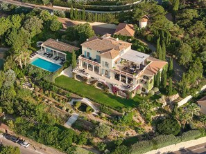Une grande maison à plusieurs étages, dotée d’une piscine, entourée d’une végétation luxuriante et d’un jardin bien entretenu.