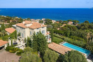 Une grande villa avec piscine, entourée d’une végétation luxuriante et offrant une vue sur la mer.