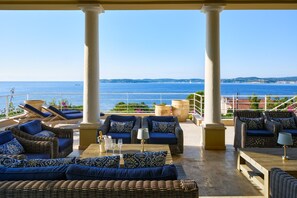 A covered outdoor seating area with wicker furniture and a view of the sea.