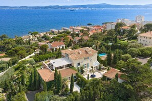 A coastal residential area with terraced houses, a large swimming pool, and a view of the sea.