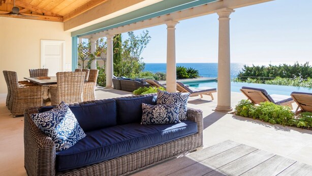 A covered outdoor seating area with wicker furniture, a pool, and a view of the ocean.