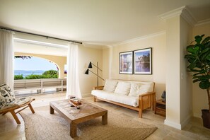 Un salon avec un canapé, une table basse et une vue sur la mer depuis un balcon.